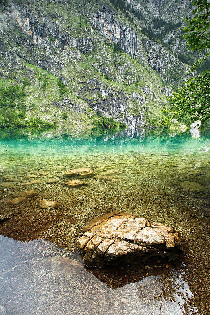 Reflection at Obersee with rock stone in the water in the background. Rocky mountain wall, Berchtesgaden National Park, Bavaria, Germany