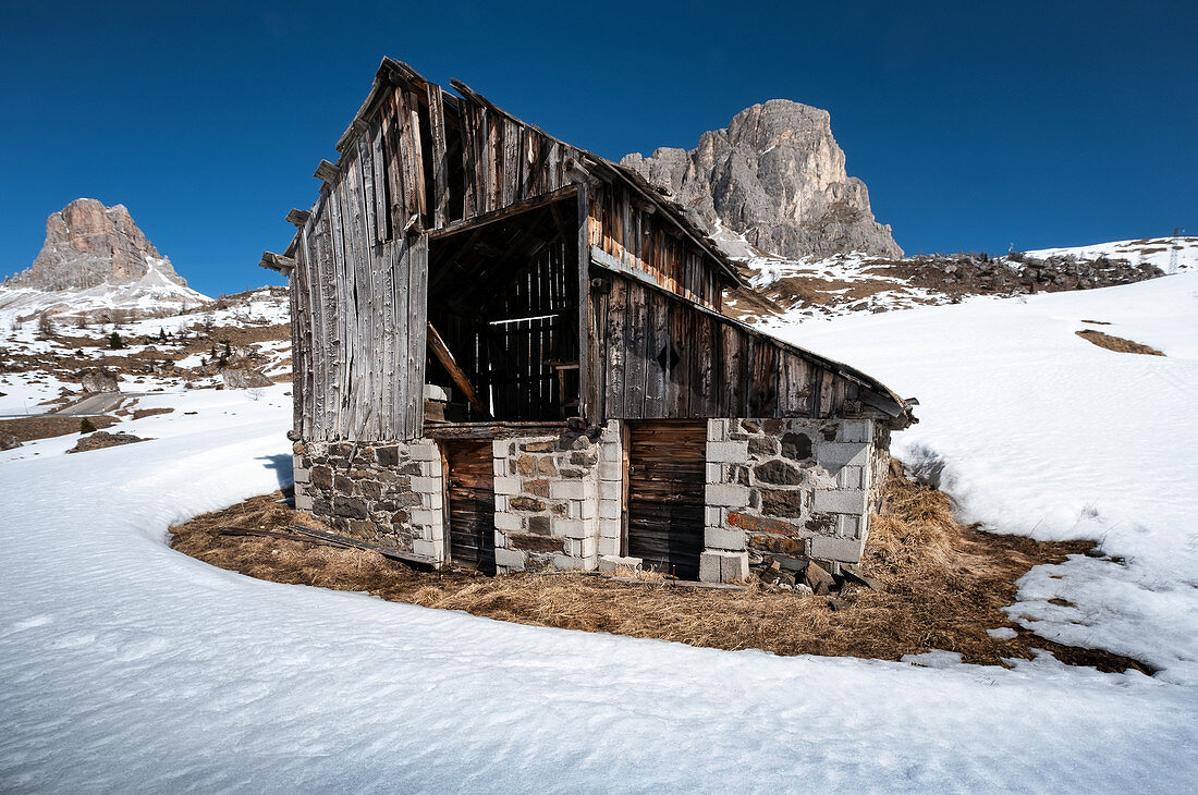 Old dilapidated wooden hut in the snow at Passo di Giau in winter. Transition to springtime, Dolomites, Cortina d'Ampezzo, Belluna, Italy