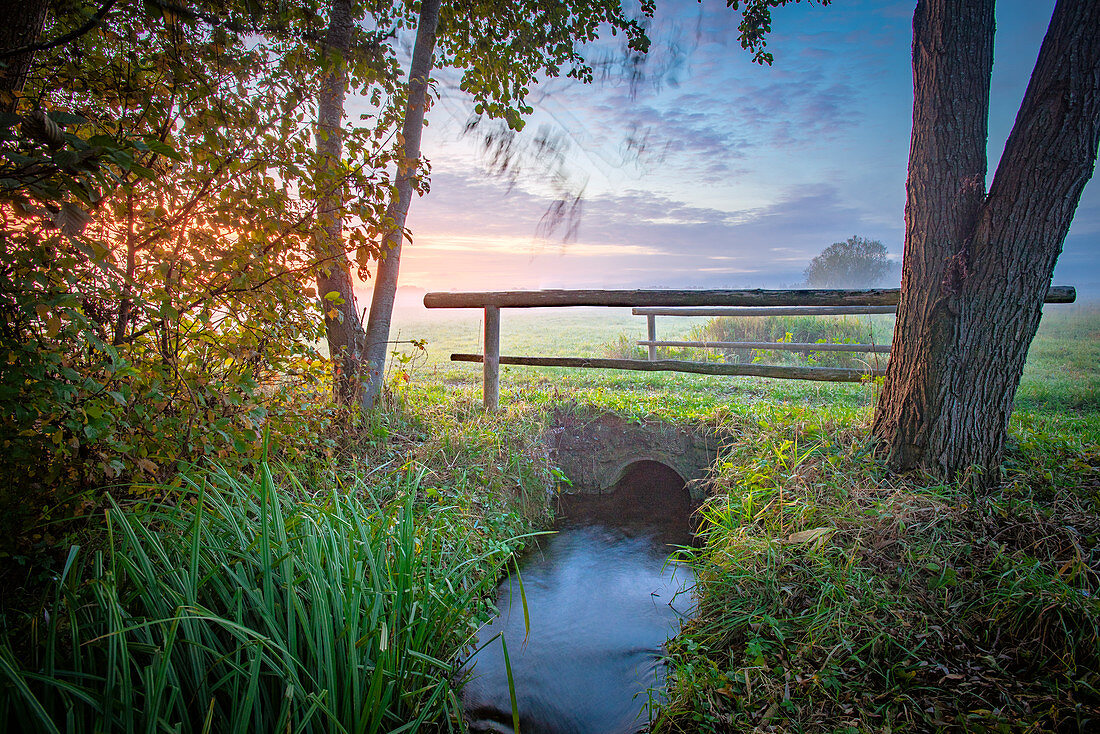 Bridge leads over small stream in the pasture in the morning mood