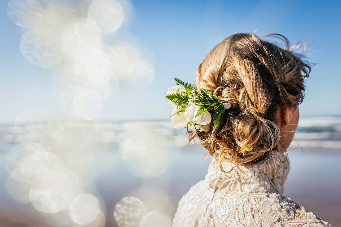 Blonde Braut mit Blumen im Haar am sonnigen Strand