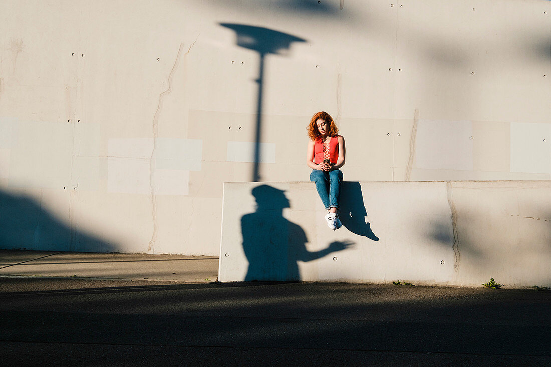 Junge Frau mit Smartphone auf Betonmauer sitzend