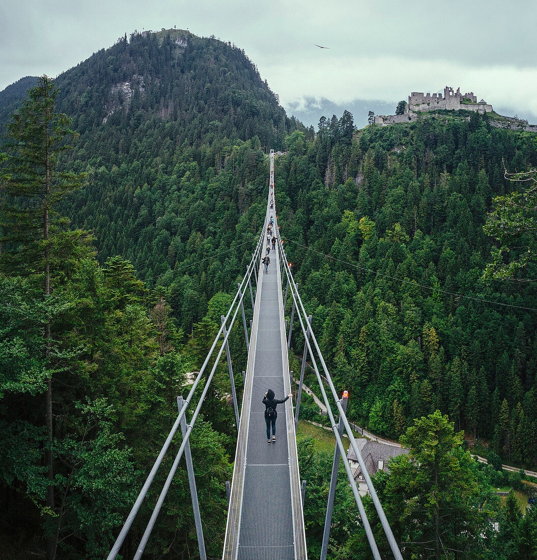 People walking across suspension bridge over green treetops, Tyrol, Austria