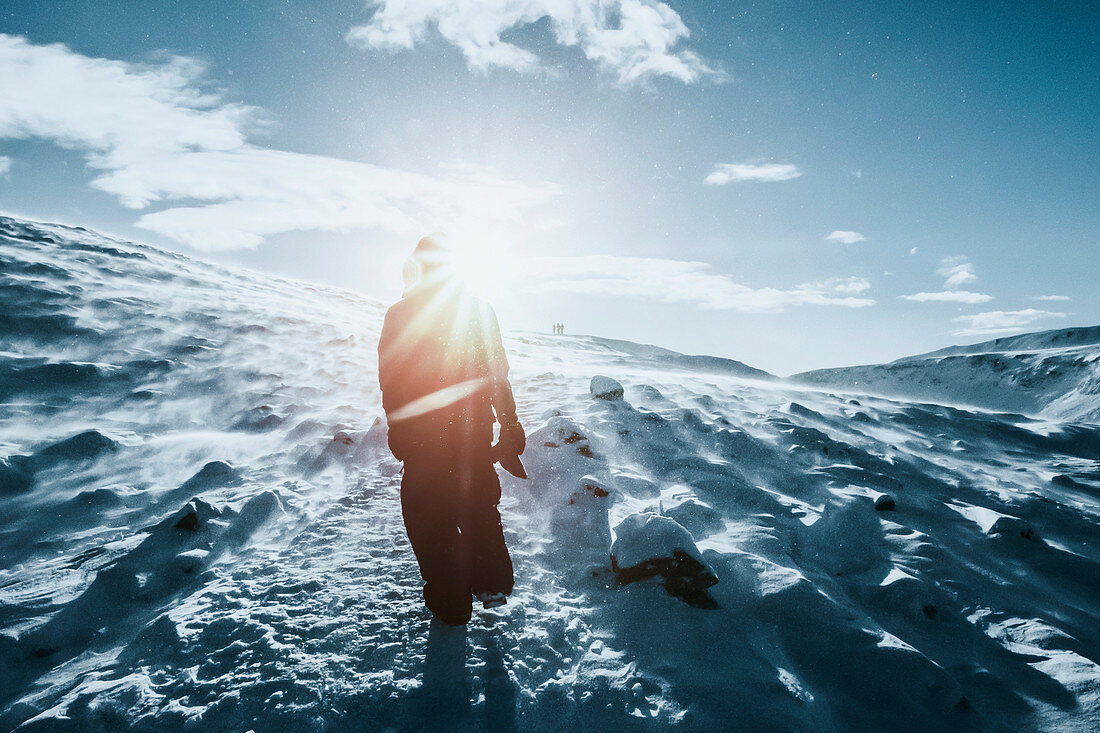 Man walking along sunny snow covered landscape, Reykjadalur, Iceland