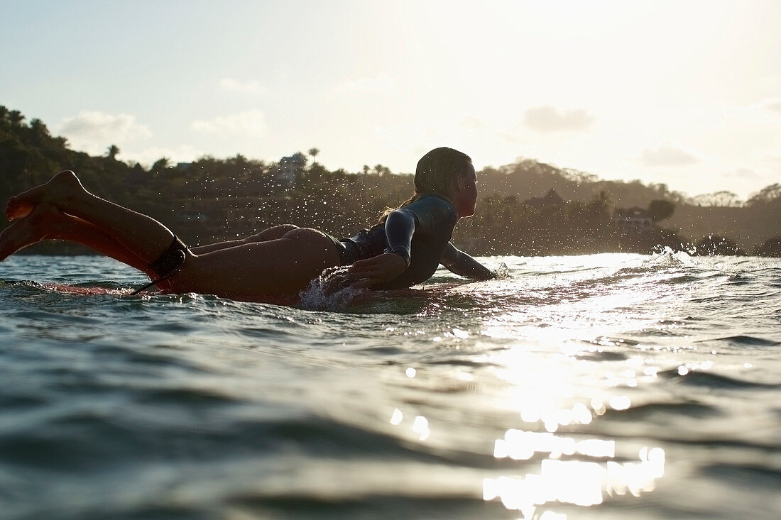 Frau auf Surfbrett liegend beim Sonnenuntergang im Meer