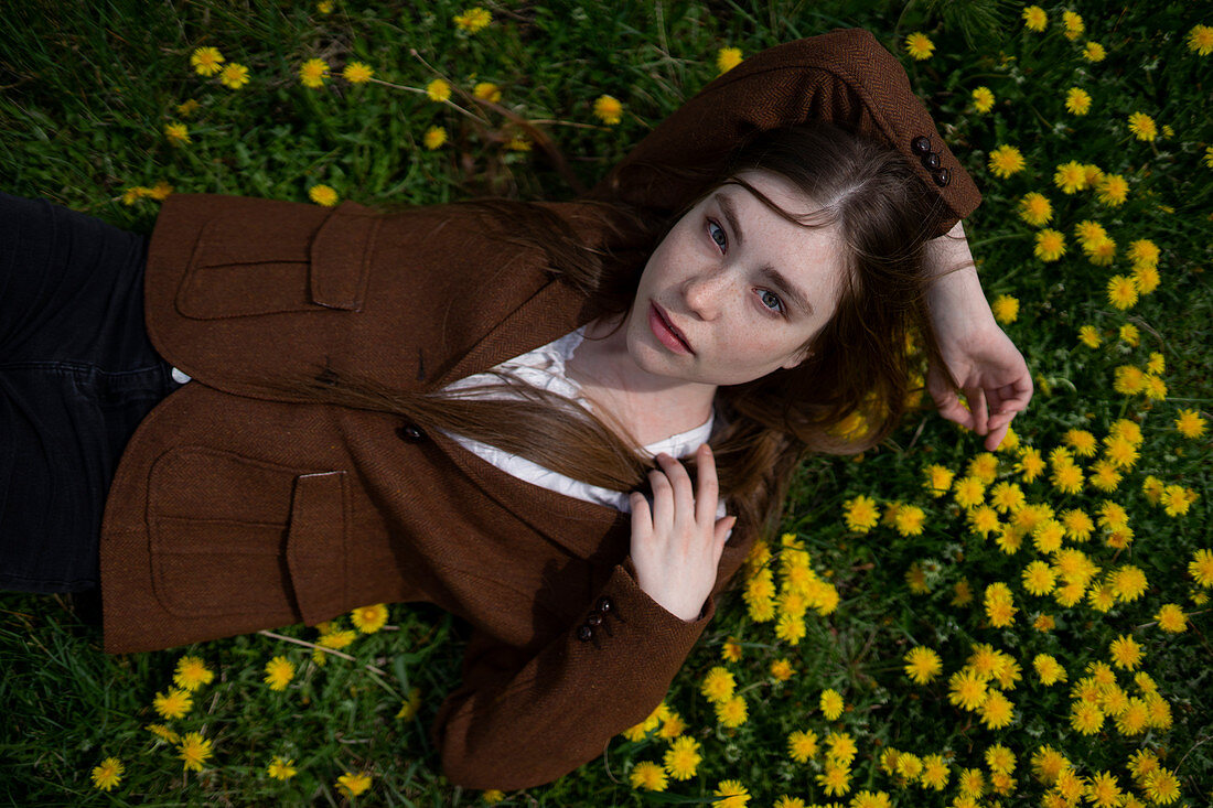 Junge Frau in braunem Blazer liegt auf Wiese mit gelben Blumen