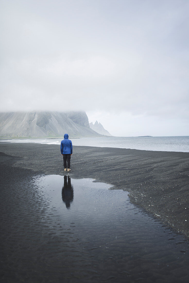 Mann in blauem Mantel am schwarzen Sandstrand in Kirkjubaejarklaustur, Island