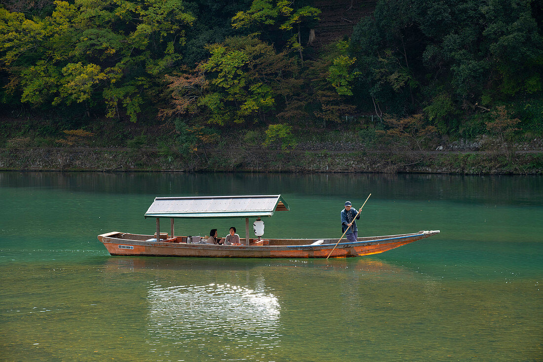 Tourists sightseeing in a small wooden boat on the Oi River in the Arashimaya region outside Kyoto, Japan, Asia