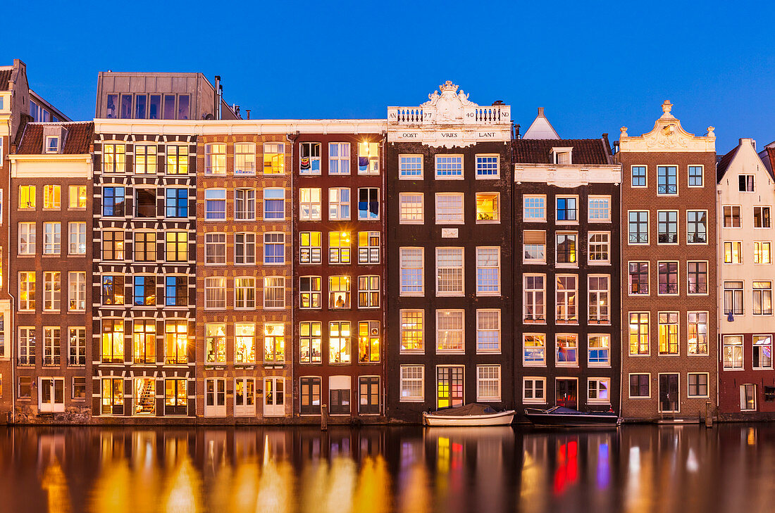 Dutch gables on row of typical Amsterdam houses at night with reflections in the Damrak canal, Amsterdam, North Holland, Netherlands, Europe