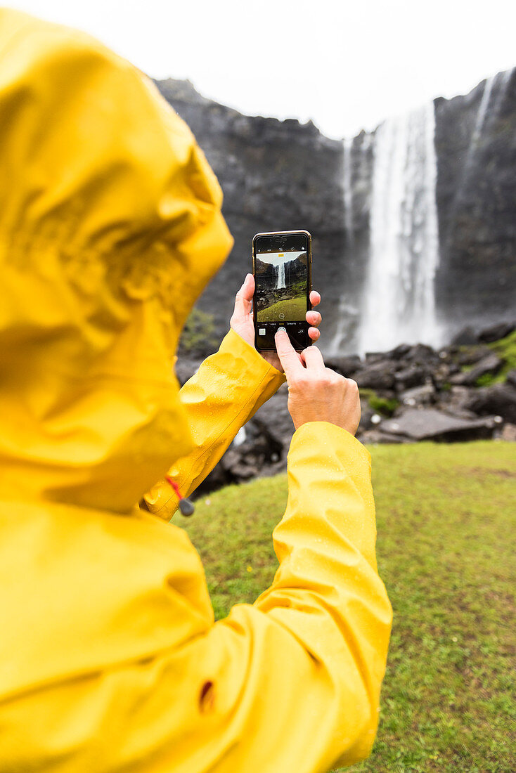 Tourist macht Fotos mit Smartphone, Fossa-Wasserfall, Streymoy-Insel, Färöer, Dänemark, Europa