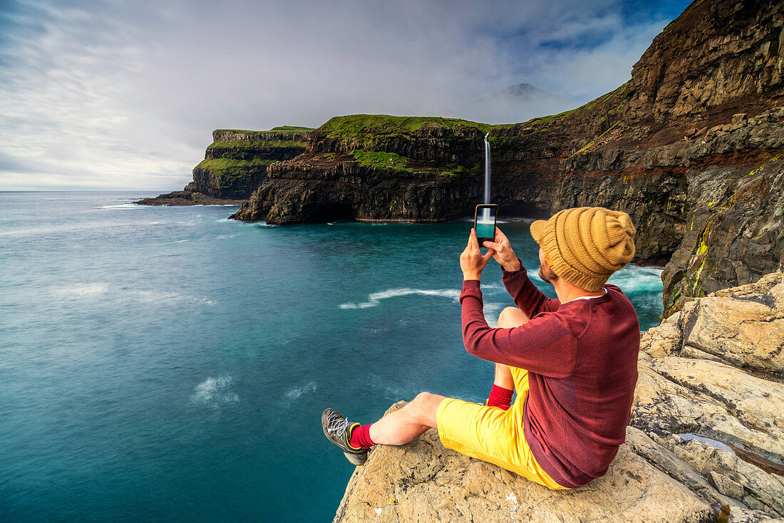 Man with smartphone snaps photos at Gasadalur waterfall, Vagar island, Faroe Islands, Denmark, Europe