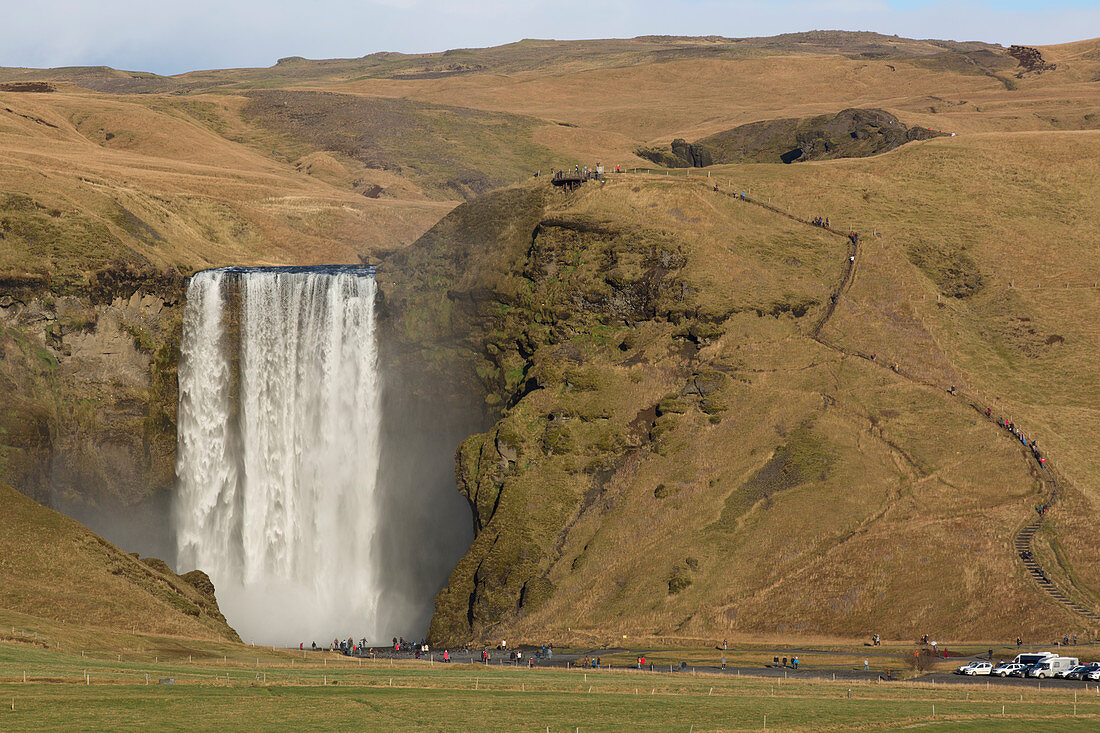 Large group of tourists standing at bottom of splashing Skogafoss waterfall, Iceland