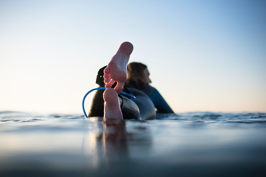 Frau im Neoprenanzug auf Surfbrett liegend