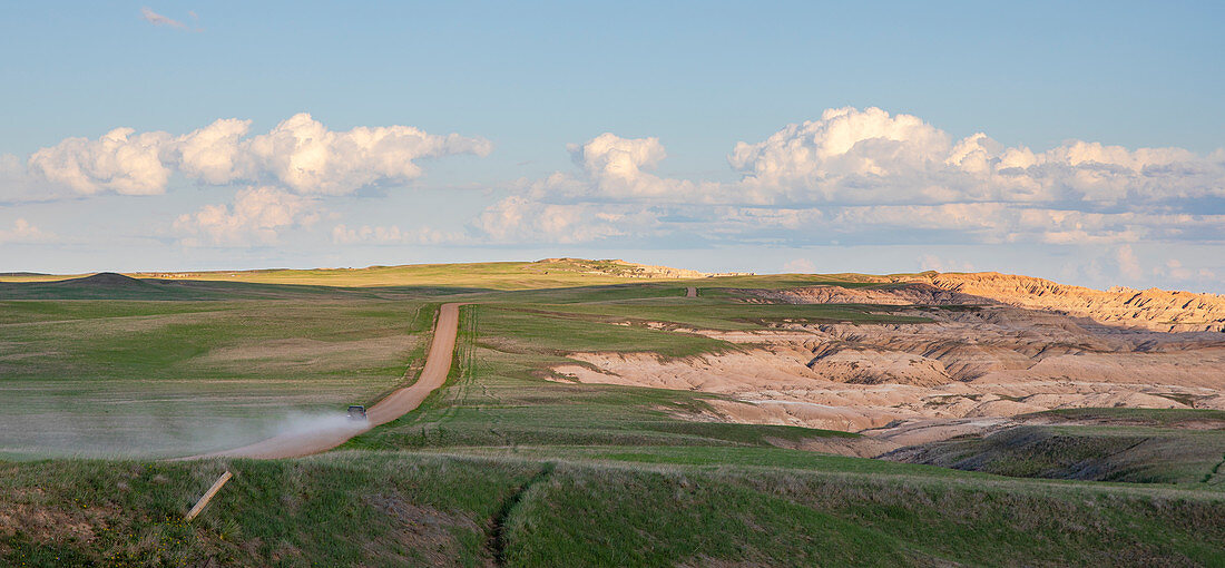 Clouds over car driving on dirt road in Badlands National Park, South Dakota, USA