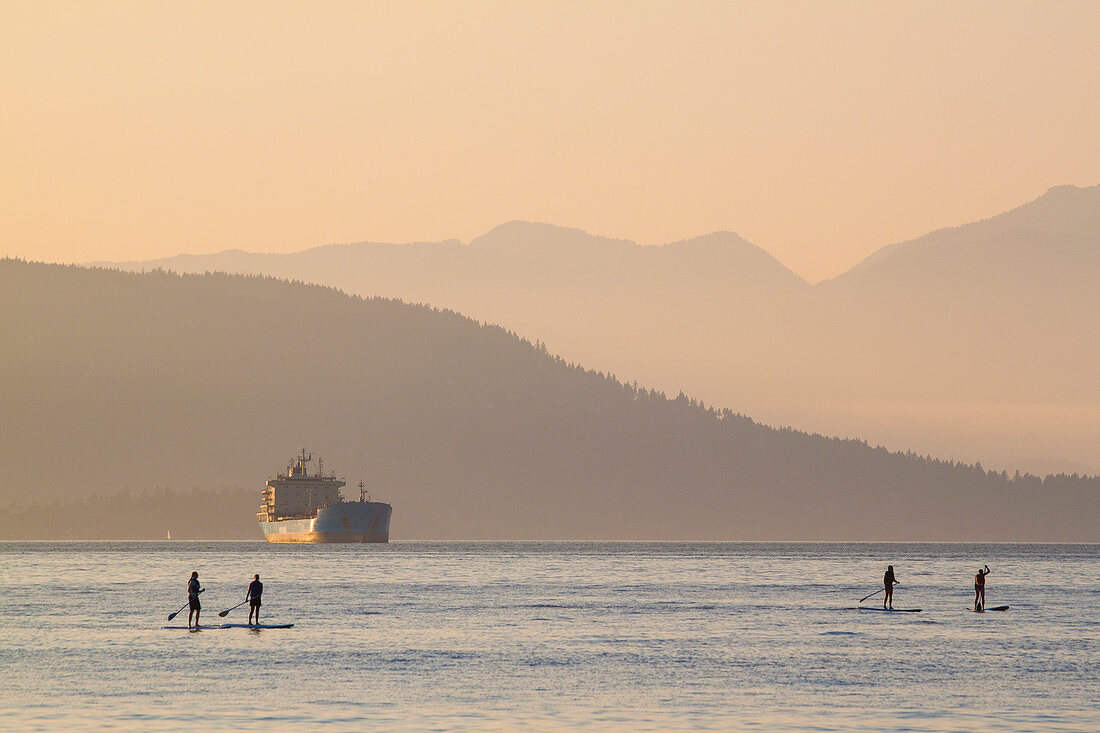 Vierköpfige Paddelboardgruppe im Meer bei Sonnenuntergang, Vancouver, British Columbia, Kanada