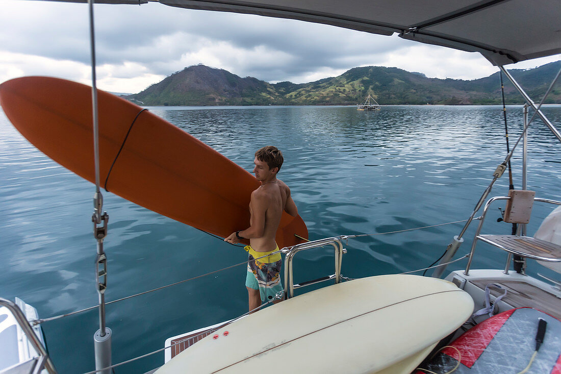 Junger Mann mit Surfbrett auf Yacht