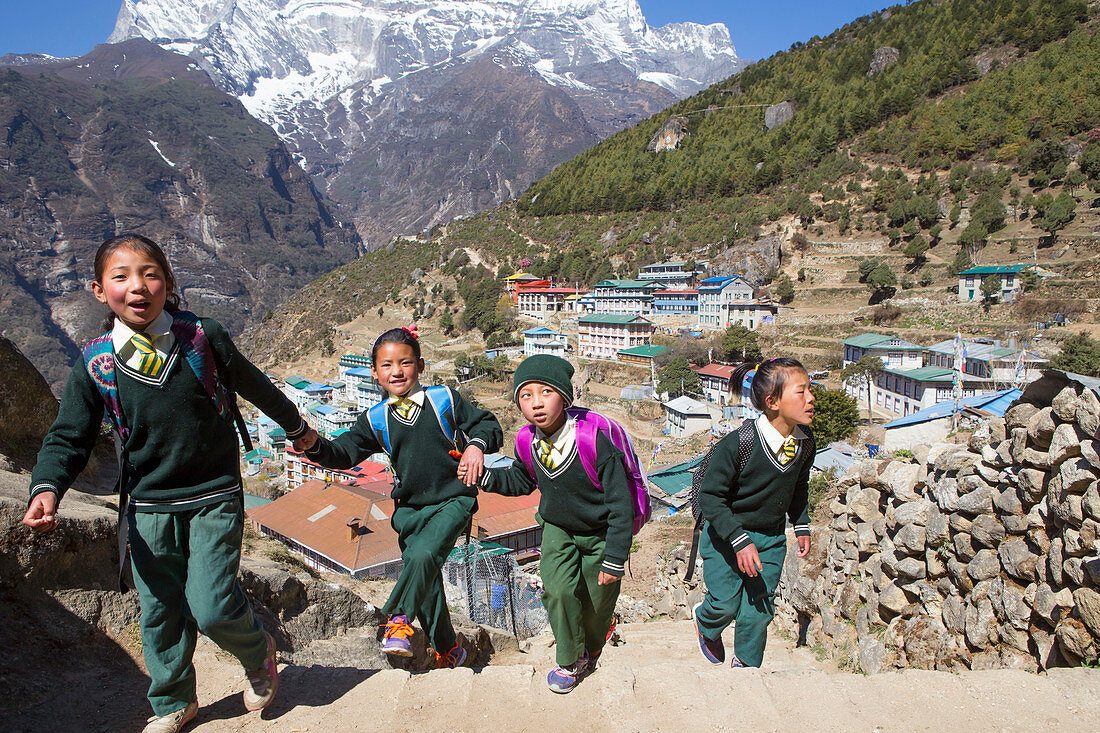 Vier kleine Kinder in Schuluniformen laufen im hügeligen Namche Bazar, einem Bergdorf im nepalesischen Khumbu-Tal