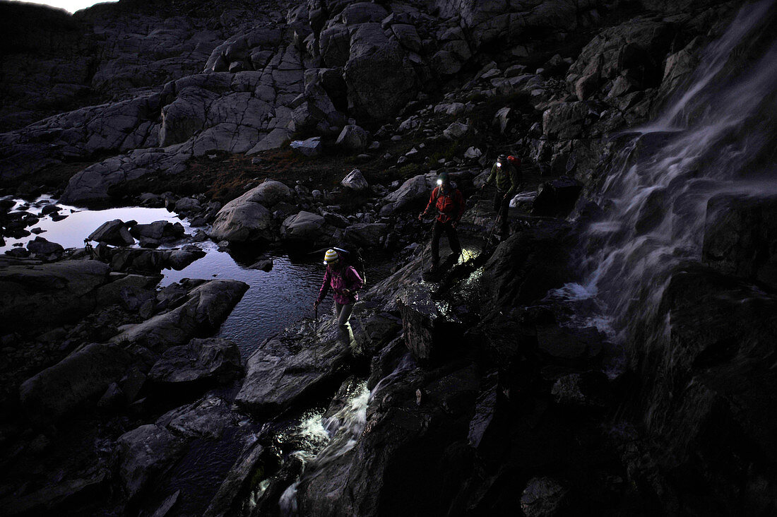 Backpackers with headlamps while passing waterfall at night near Mt Ritter on trek of Sierra High Route in Minarets Wilderness, Inyo National Forest, California, USA
