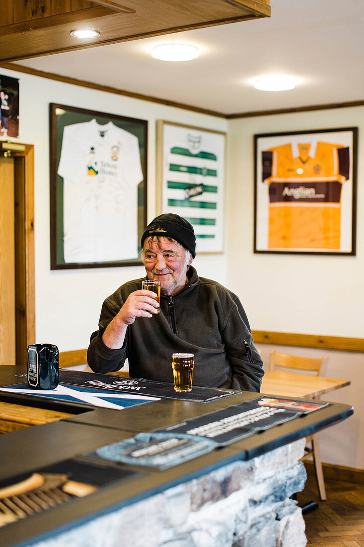 Older man enjoying beer beside counter at pub, Scotland, UK