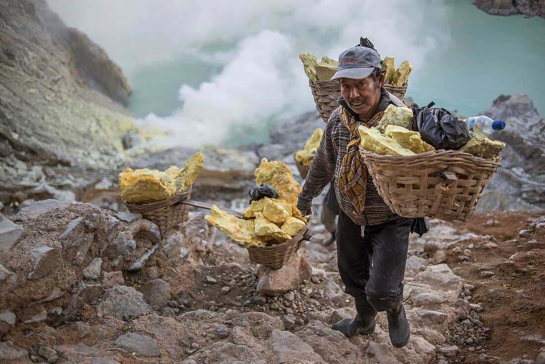 Bergmann trägt schwere Körbe mit Schwefelgesteinen, am Vulkan Kawah Ijen, Ost-Java, Indonesien