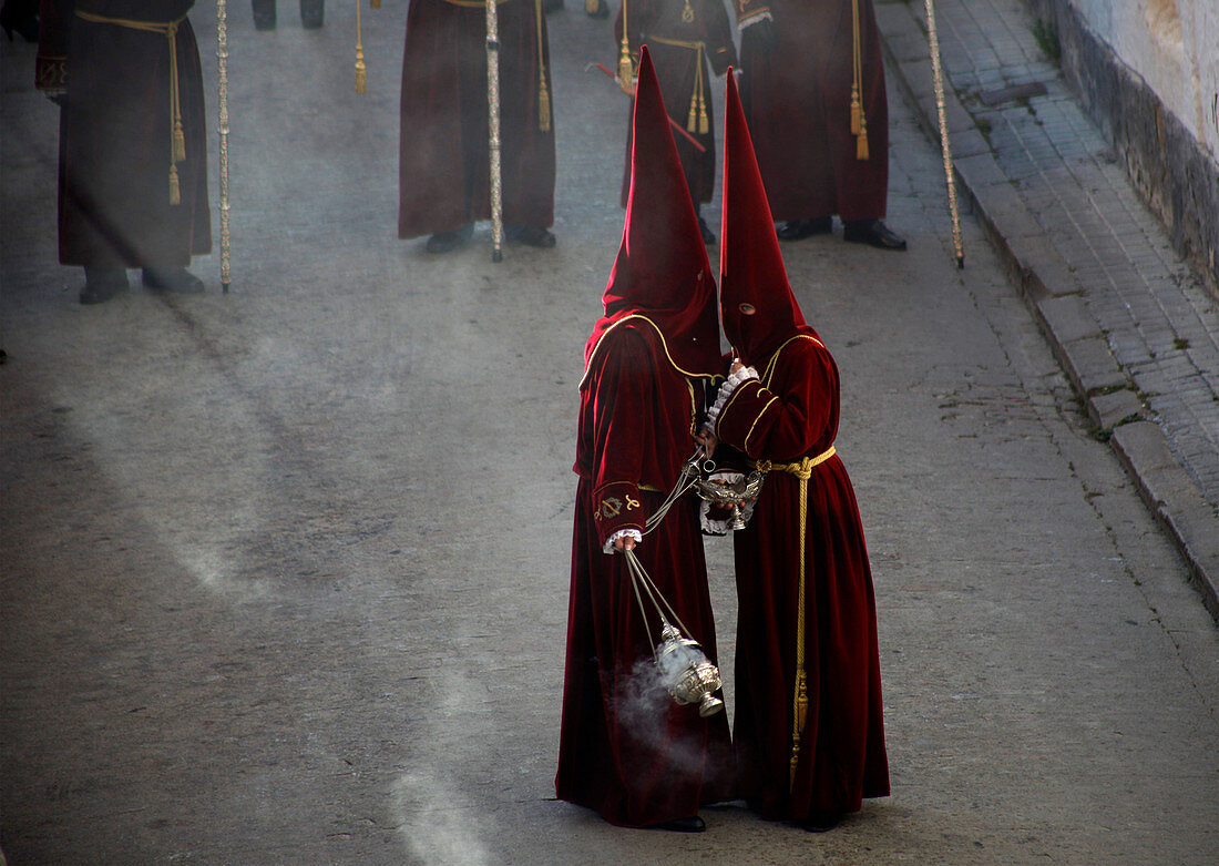 Altar servers wearing red clothing and pointed hoods talking during Easter Week celebrations in Baeza, Jaen Province, Andalusia, Spain