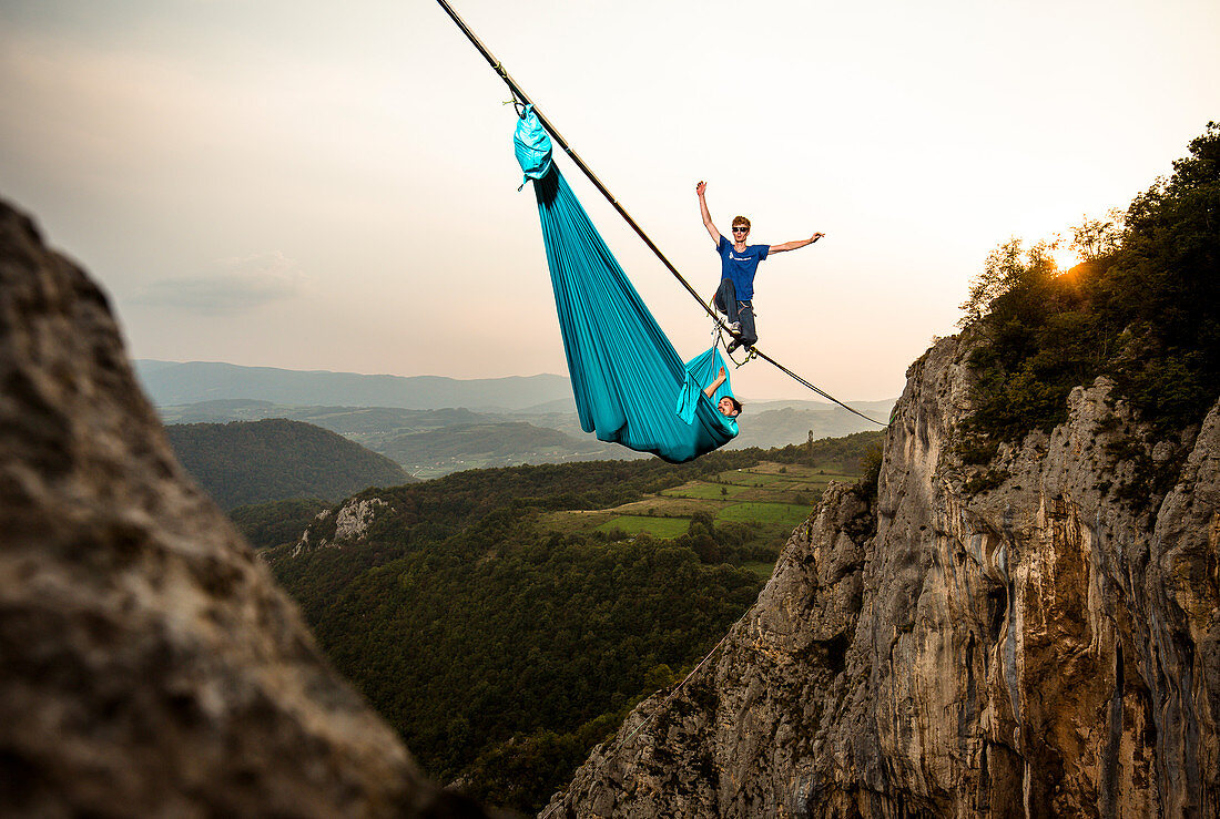 Highline athlete walking on slackline in mountains while his fellow hanging in hammock, Tijesno Canyon, Banja Luka, Bosnia