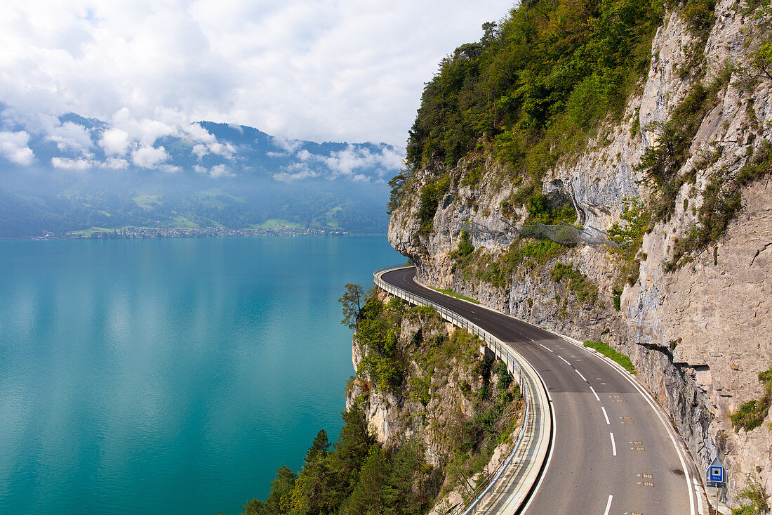 A curved road built into the side of a mountain next to Lake Thun, Interlaken, Bernese Oberland, Bern, Switzerland, Europe