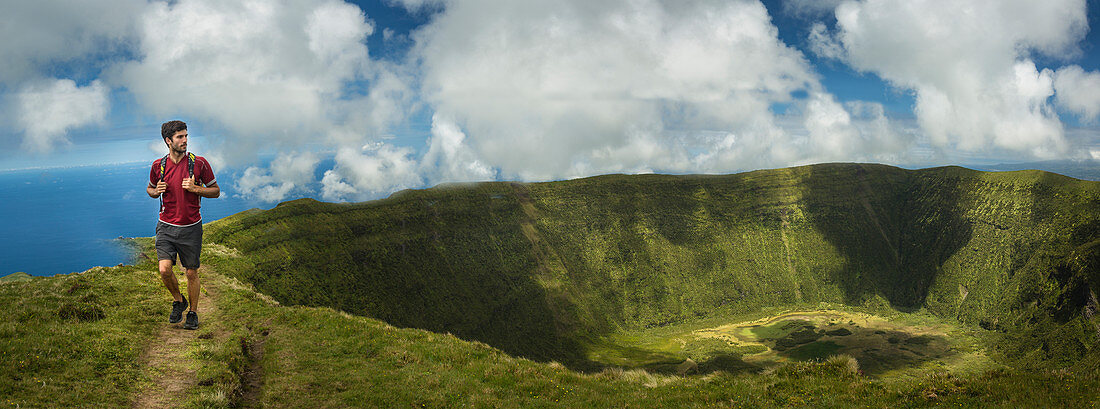 Hiker walking on hilltop dirt path over Cabeco Gordo crater, Faial, Portugal