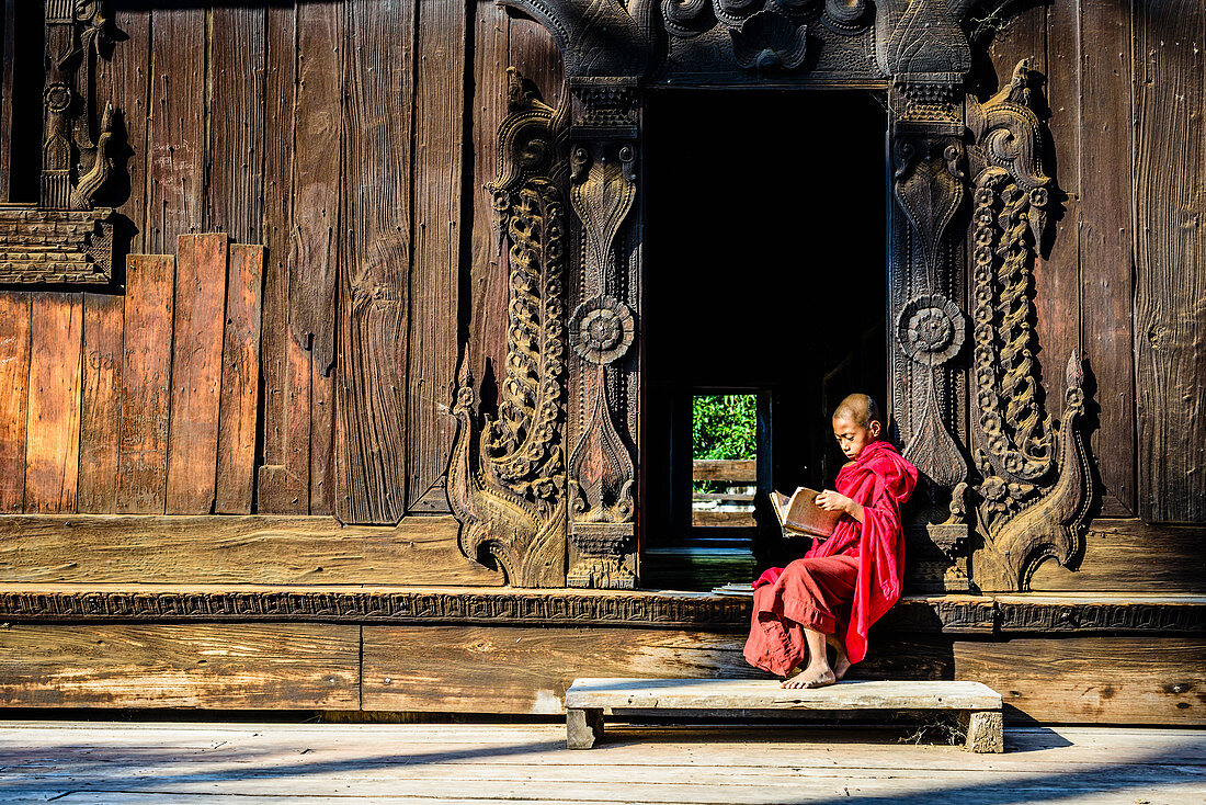 Asiatischer Mönch beim Lesen am verzierten Eingang zum Tempel, Myanmar