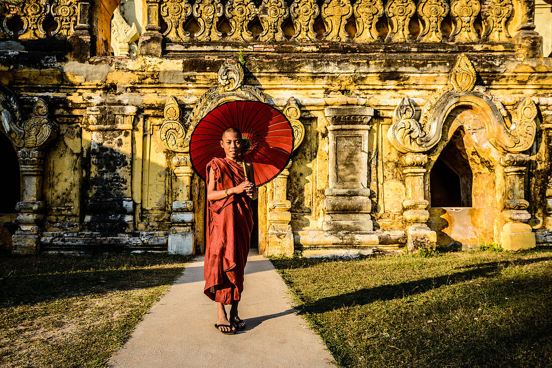 Asiatischer Mann mit Regenschirm bei verziertem Tempel, Myanmar