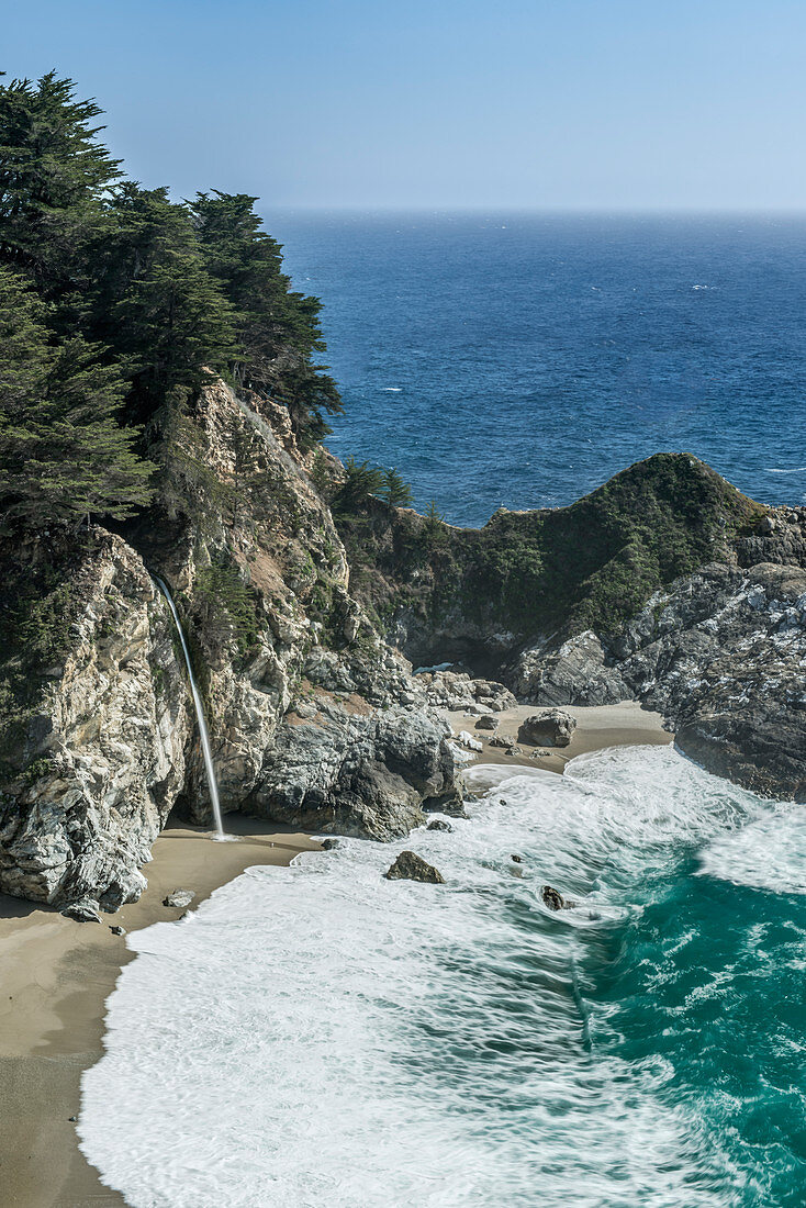 Waterfall pouring into waves washing up on rocky beach, USA