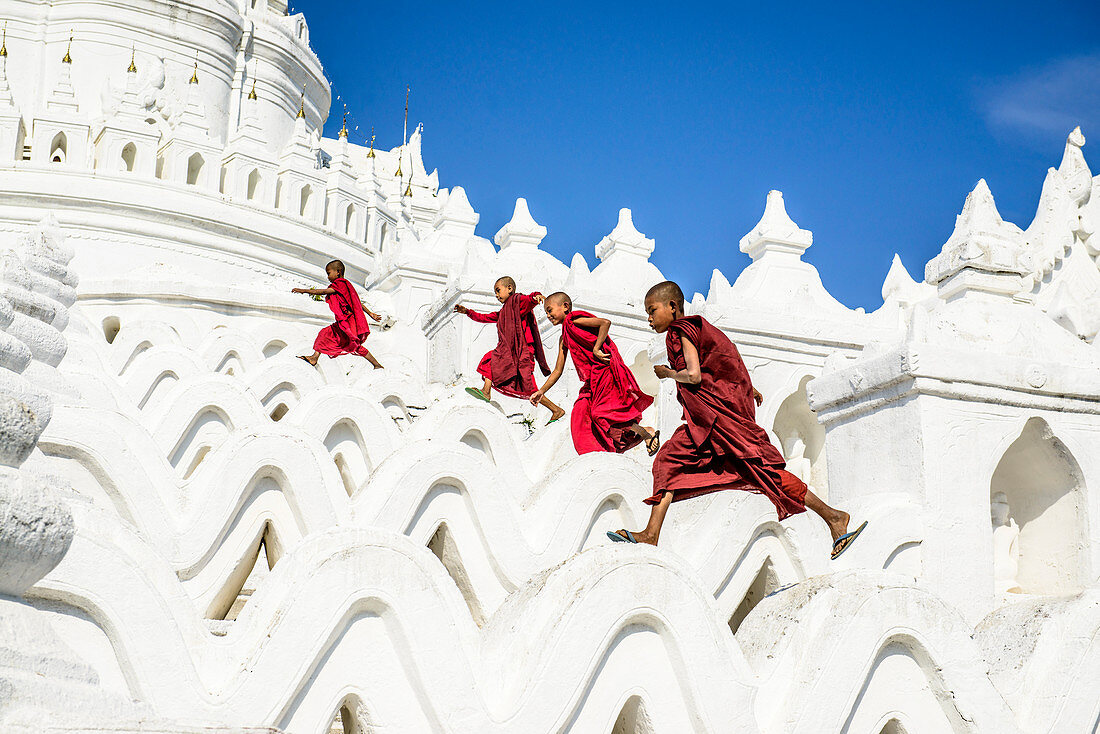 Asiatische Mönche laufen auf weißen Tempelwänden, Hsinbyume Pagode, Mandalay, Sagaing, Myanmar