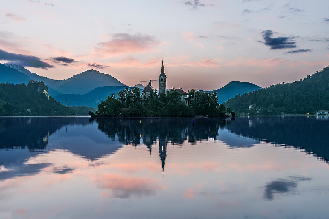 Dorfkirche und Gebäude spiegeln sich nachts in einem ruhigen See, Bled, Oberkrain, Slowenien