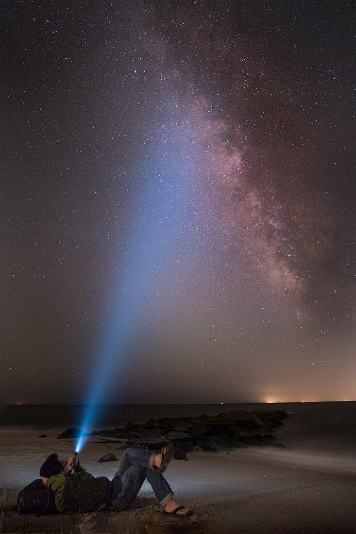 Asian man shining flashlight on starry sky, Cape May, New Jersey, USA