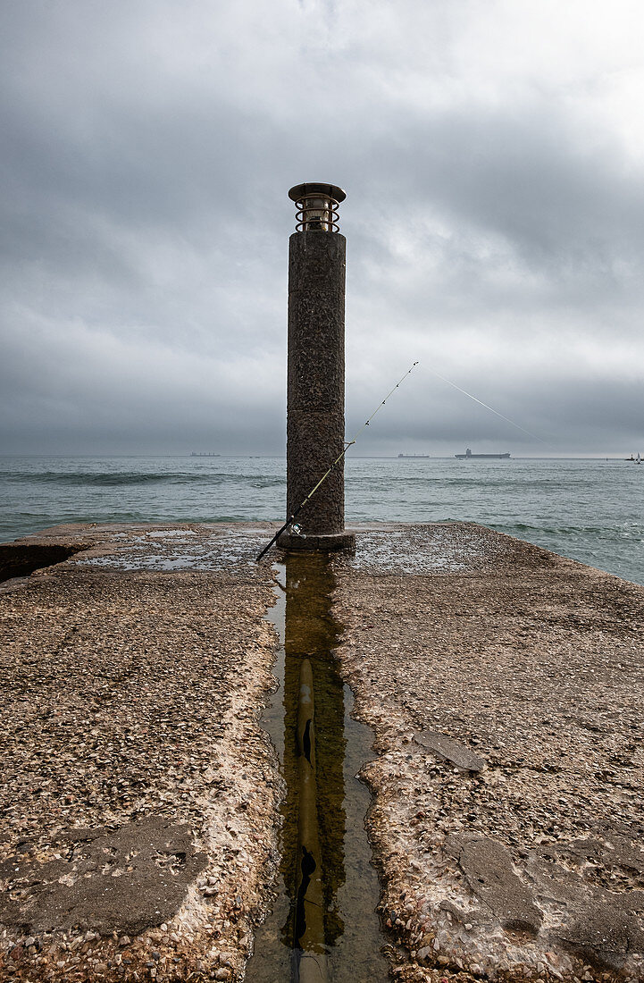 Angel am Leuchtturm auf betoniertem Steg, Praia das Moitas, Cascais, Portugal