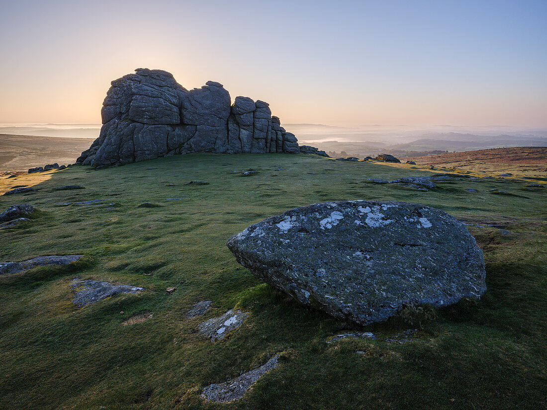 Sonne hinter Granitfelsen bei Haytor im Dartmoor Nationalpark und entfernter Nebel im Teign Valley, Bovey Tracey, Devon, England, Großbritannien, Europa