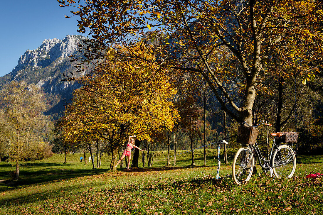 Young woman on a slackline stretched between autumn colored trees, Kiefersfelden, Bavaria, Germany