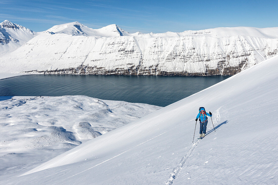 Skitourengeherin im Aufstieg, im Hintergrund ein Fjord auf der Halbinsel Tröllaskagi, Island