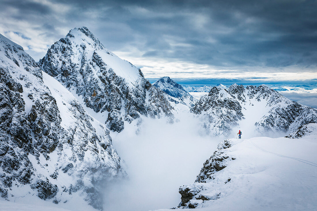 Skitourengeher steht auf einem Vorsprung in der Mieminger Kette vor majestätischer Gebirgskulisse mit mystischer Wolkenstimmung, Tirol, Österreich
