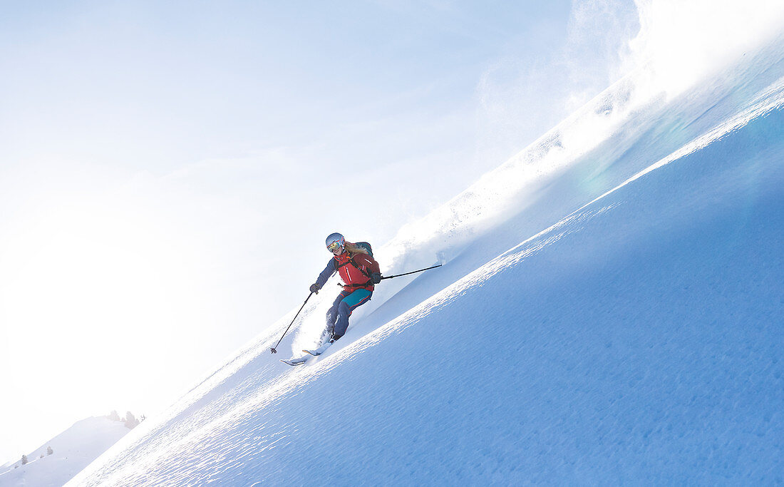 Ski touring goes backlit against the low sun through an untouched powder slope, Kitzbüheler Alpen, Tyrol, Austria