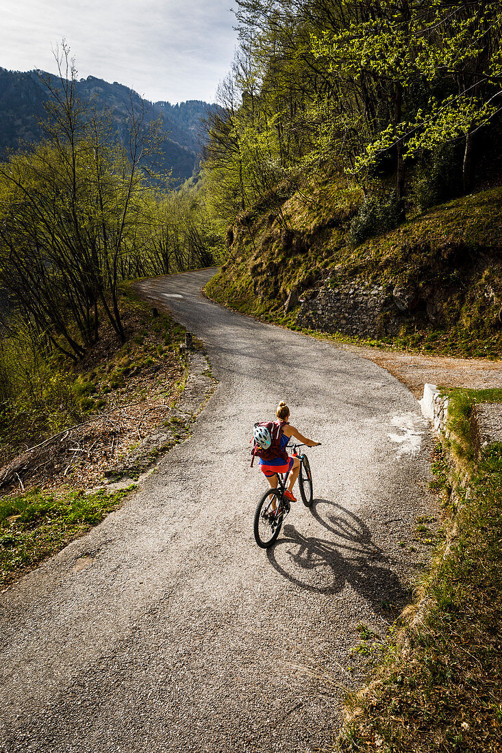 Young woman rides a mountain bike up a narrow asphalt road, Lake Idro, Italy