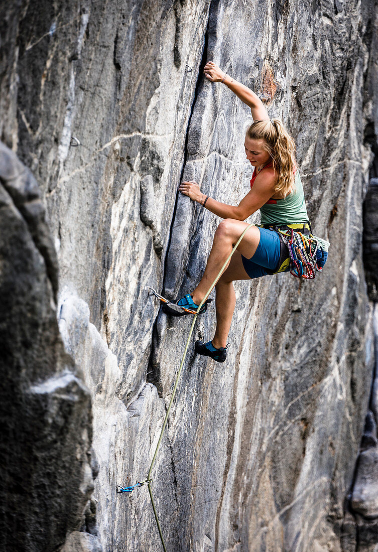Junge blonde Frau klettert im Vorstieg in einer überhängenden Granitwand, Maltatal, Kärnten, Österreich