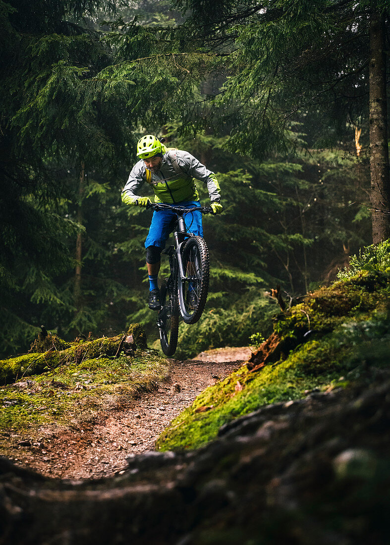 In bad weather, mountain biker jumps with an Enduro e-bike over a small hill, Kitzbüheler Alpen, Tyrol, Austria