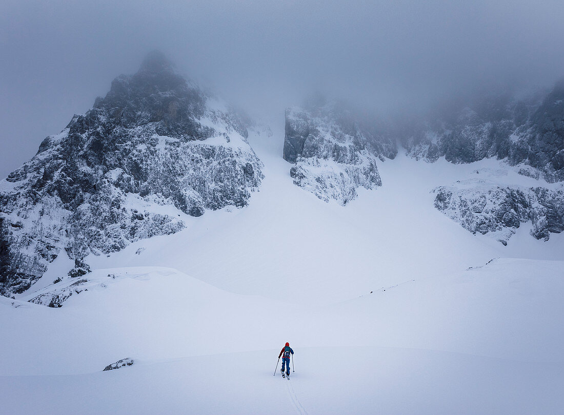 Skitourengeher im Aufstieg zu einer steieln Rinne bei schlechter Sicht und wolkenverhangen Bergen, Wilder Kaiser, Tirol,