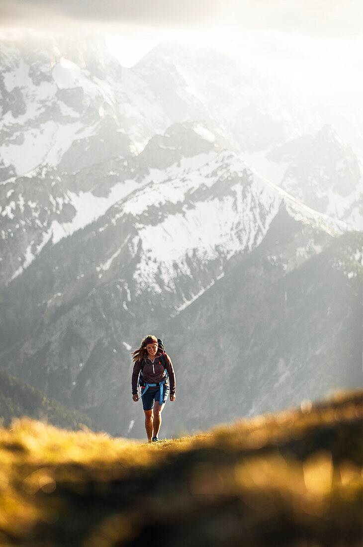 Young blonde woman in shorts hiking in wonderful warm back light with snowy mountains in the background, Hinterriss, Karwendel, Tyrol, Austria