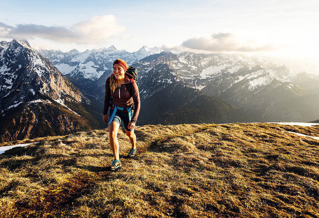 Junge blonde Frau in kurzer Hose beim Wandern in herrlichen warmen Gegenlicht  mit verschneiten Bergen im Hintergrund, Hinterriss, Karwendel, Tirol, Österreich