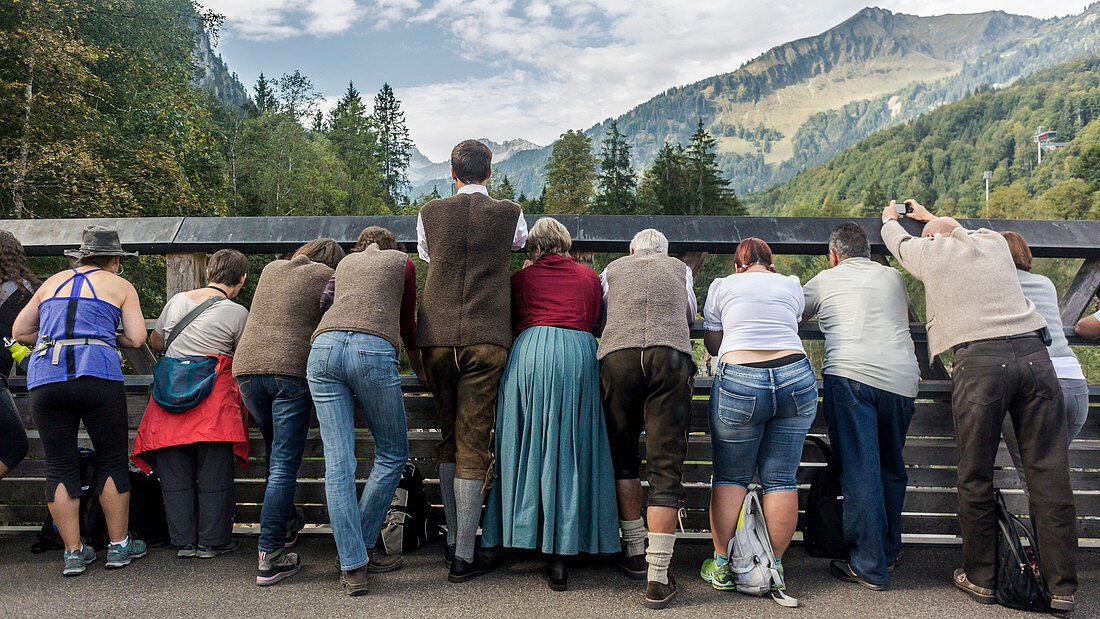 Menschengruppe steht erwartungsvoll auf einer Brücke in den Bergen, Deutschland, Bayern, Allgäu 