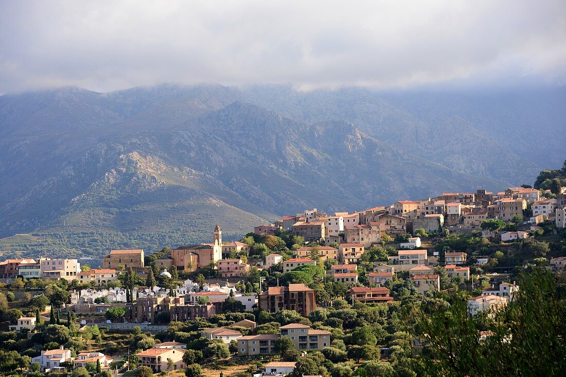 Wolkenverhangene Berge mit dem Bergdorf Curbara in der Balagne, Nord- Korsika, Frankreich