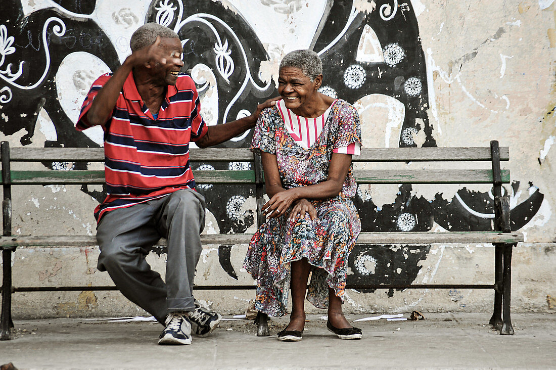 2 friends are chatting and laughing on a street bench in the capital of Cuba. Havana