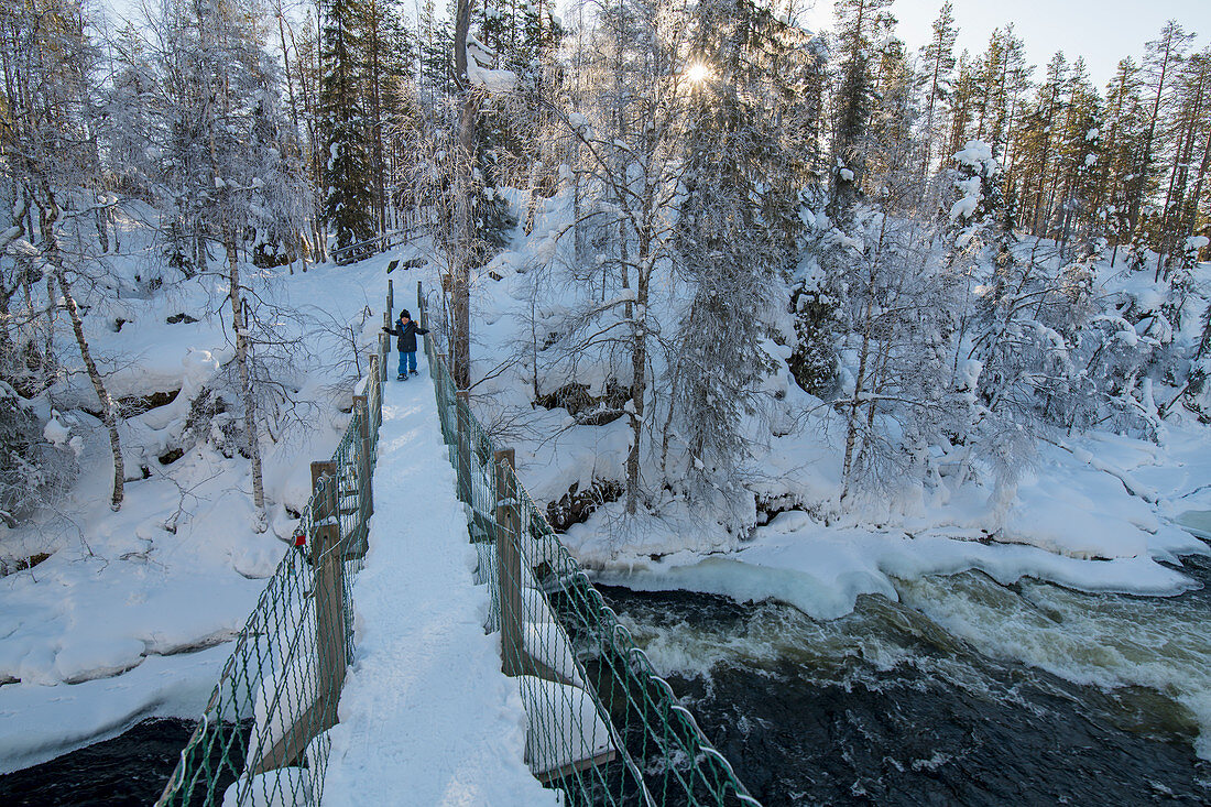Kleiner Junge stapft mit Schneeschuhen über eine Brücke, Winterwald, Finnland