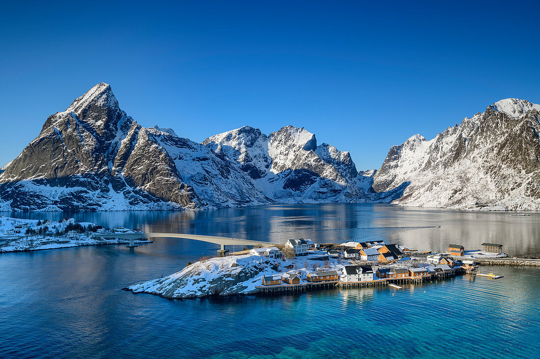 Insel bei Hamnoy mit norwegischen Häusern, verschneite Berge im Hintergrund, Hamnoy, Lofoten, Nordland, Norwegen